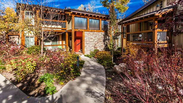 A modern two-story house with a stone facade, a wooden deck, and a well-maintained garden. - Willows Condos by Snowmass Vacations (Snowmass Village)