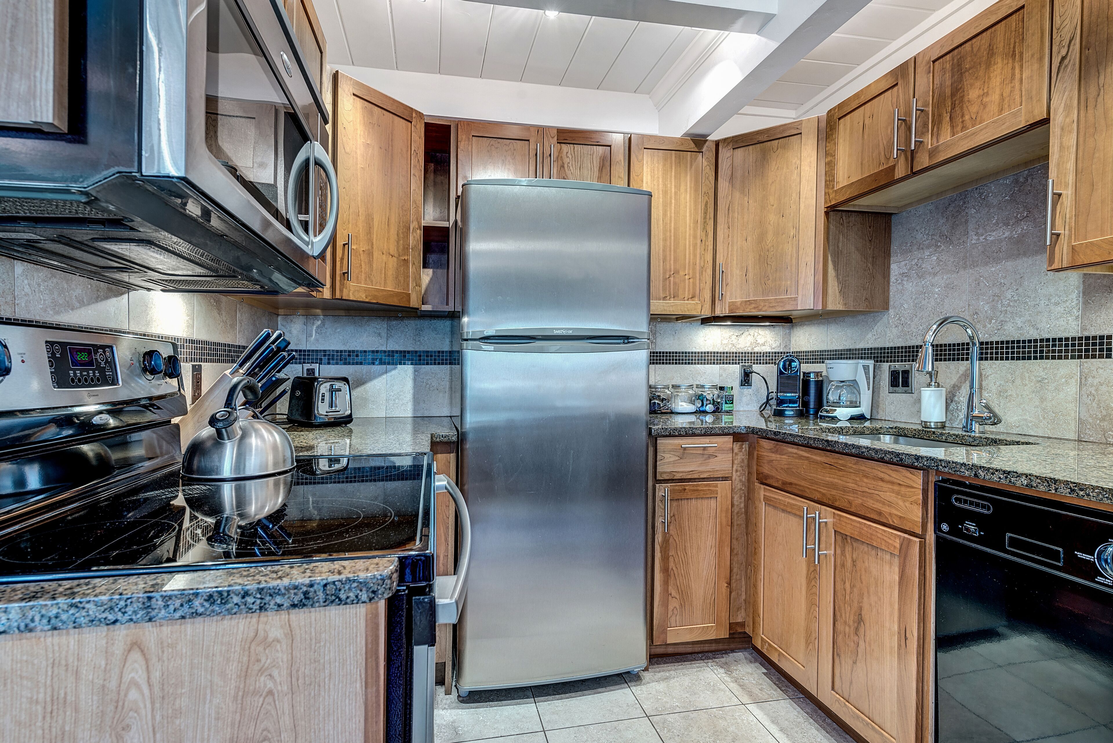 A modern kitchen with stainless steel appliances, wooden cabinets, and a tiled backsplash.