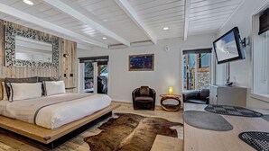 A modern bedroom with a large bed, a wooden headboard, a mounted TV, and a view of the outdoors. - Willows Condos by Snowmass Vacations (Snowmass Village)
