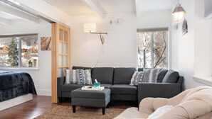 A modern living room with a sectional sofa, a beige armchair, a small ottoman, and a large window offering a view of a snowy landscape. - Willows Condos by Snowmass Vacations (Snowmass Village)