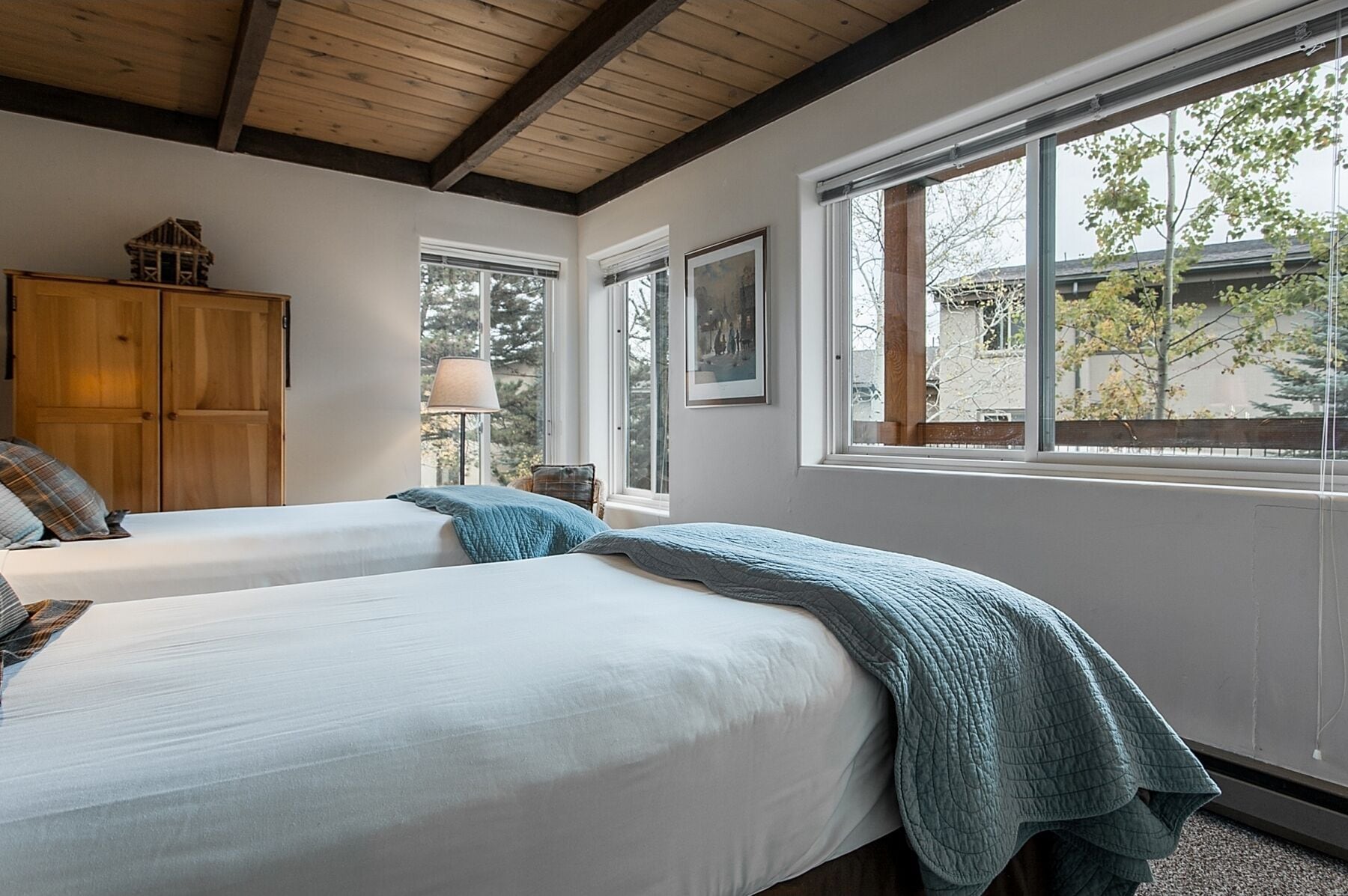 A bedroom with two beds, wooden wardrobe, large windows, and a view of the outside.