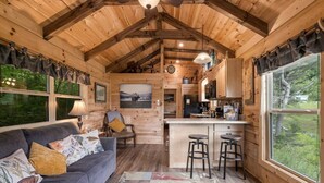 Interior de una cabaña con sala de estar, cocina y ventanas grandes.