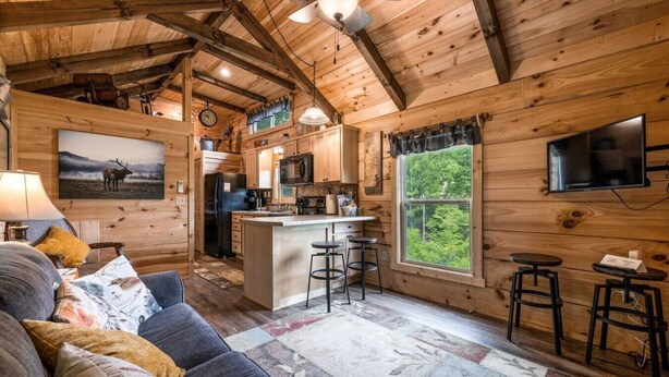 Interior rústico de una cabaña con sala de estar, cocina y taburetes de bar.