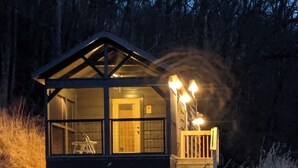 Una cabaña con frente de vidrio, puerta de madera y un porche con luces.