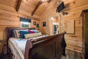 Un dormitorio de cabaña de madera con una cama, una ventana, un televisor y una puerta.