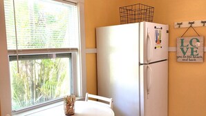 Une cuisine avec un réfrigérateur blanc, une fenêtre avec des stores, une table avec des chaises et un mur orné d’un panneau indiquant le mot « AMOUR ».