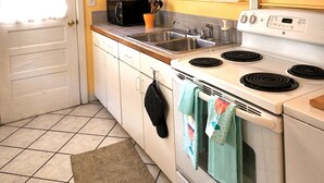 Une cuisine de taille réduite avec des meubles blancs, un évier à deux bacs, une cuisinière et un four à micro-ondes.