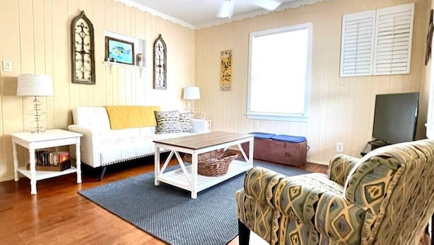 Un salon avec un canapé blanc, un fauteuil à motifs, une table basse en bois et un ventilateur de plafond.