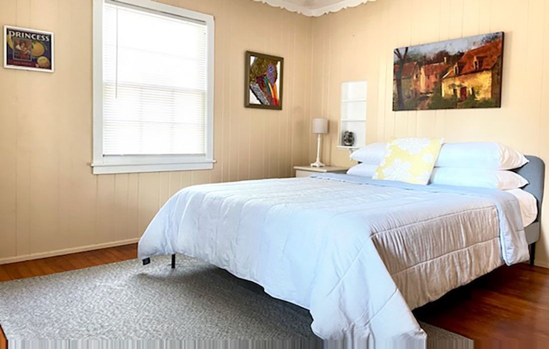 Un dormitorio con cama, mesita de noche, lámpara y un cuadro en la pared.