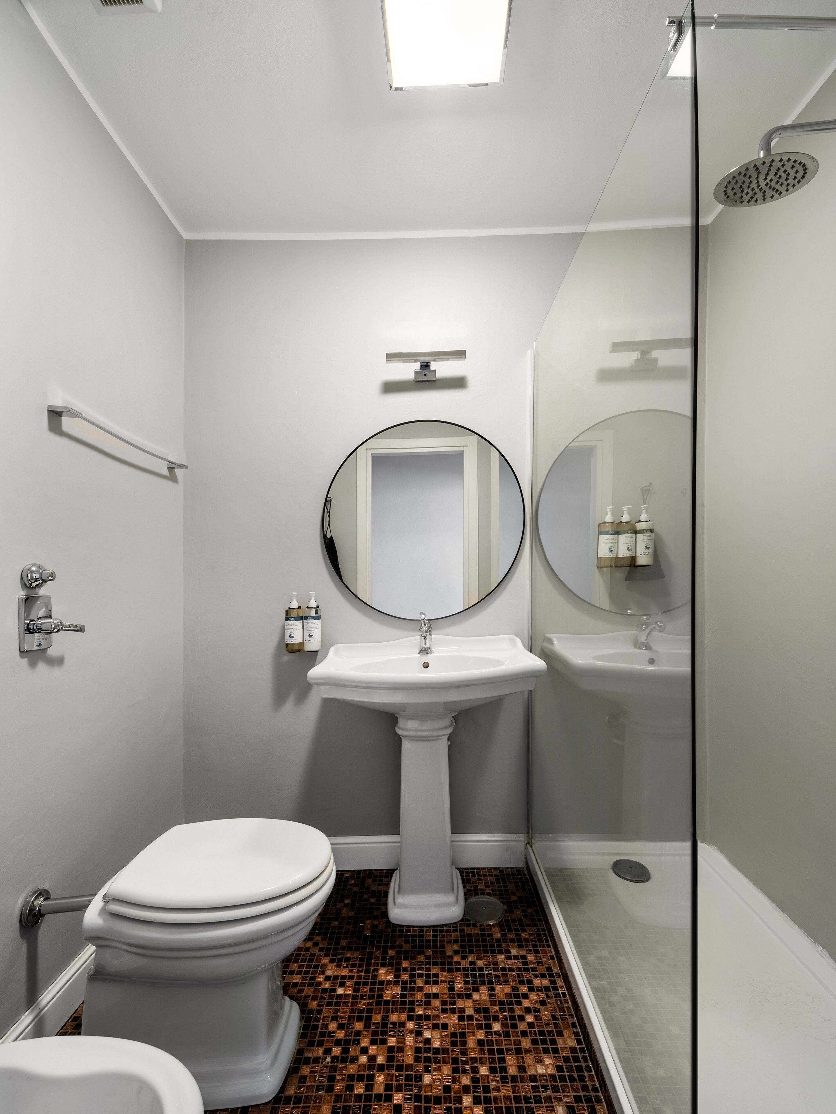 Une salle de bain avec un lavabo sur colonne, des toilettes, une douche et un miroir.