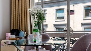 Una camera moderna con tavolo in vetro, due sedie, un piccolo frigorifero, una bottiglia d'acqua e un vaso con fiori.