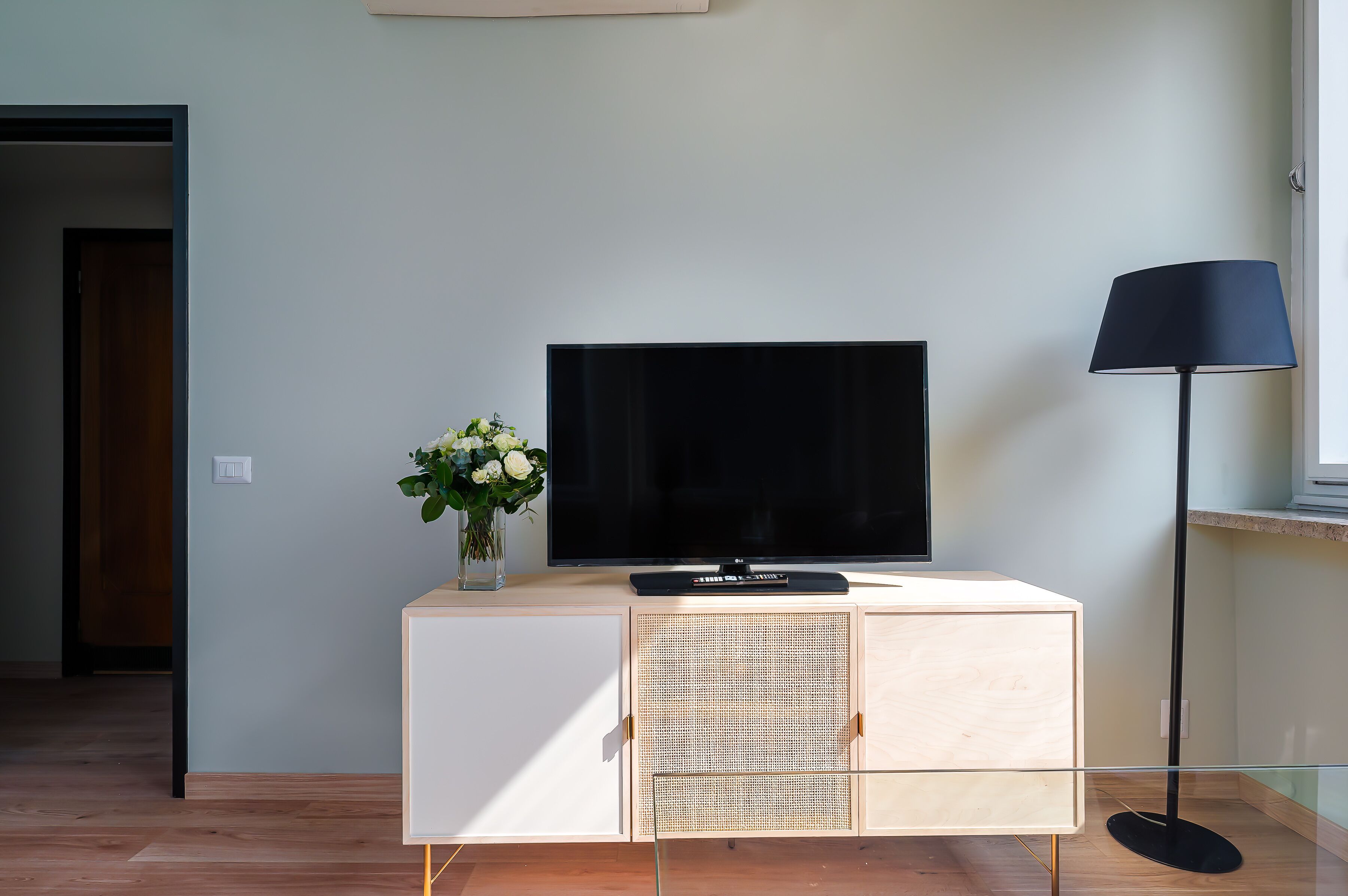 Ein modernes Wohnzimmer mit einem Flachbildfernseher auf einer Holzkommode, einer Vase mit Blumen und einer Stehlampe.