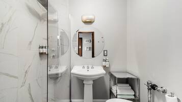 Une salle de bain moderne avec une douche à parois de verre, un lavabo sur colonne, des toilettes et un porte-serviettes.