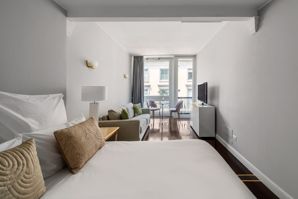 Moderni hotellihuone, jossa on suuri sänky, sohva, televisio ja parveke, jolta on näkymä kaupunkiin.