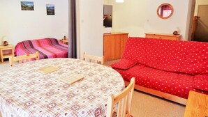 A cozy room with a round dining table, a red sofa, a wooden cabinet, and a mirror on the wall. - 50m from resort center, 1st floor, balcony, parking, tv, ski locker, 47m², Les 2 Alpes (Les Deux Alpes)
