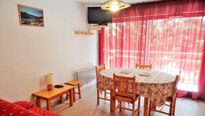 A cozy room with a dining table, chairs, a TV, and a red sofa. - 50m from resort center, 1st floor, balcony, parking, tv, ski locker, 47m², Les 2 Alpes (Les Deux Alpes)