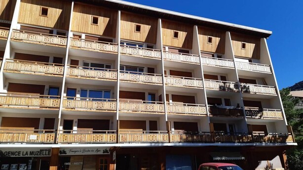 A multi-story building with balconies, a ground-level shop, and parked cars.