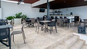 An outdoor dining area with multiple tables and chairs, a bar counter, and potted plants. - Icaro - With Rooftop At Ipana Condos (Playa del Carmen)