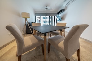 A modern dining area with a dark table and four beige chairs, a floor lamp, and a large window with a view of buildings.