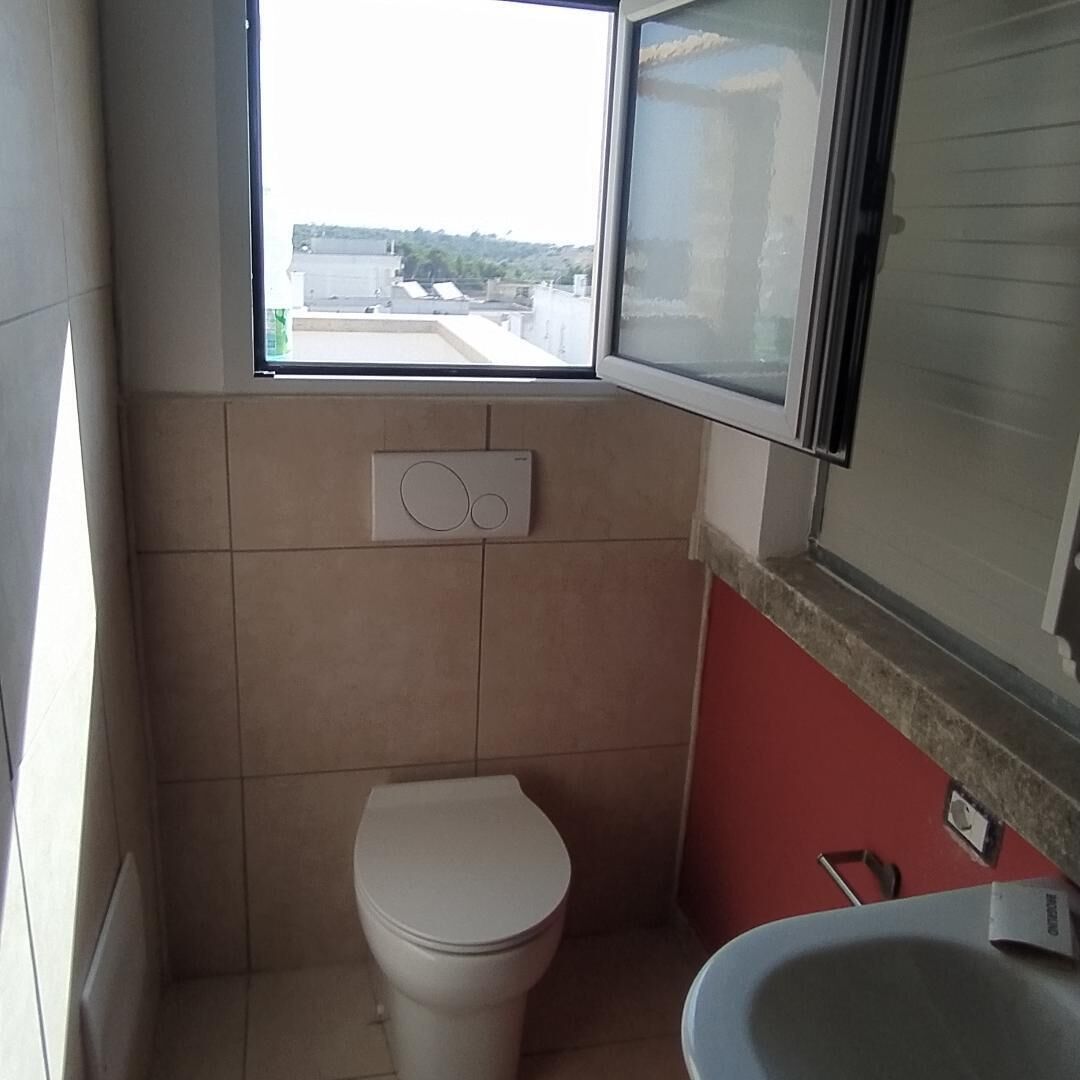 A small bathroom with a toilet, a window, and a sink.