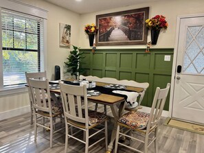 Un coin repas avec un mur recouvert de panneaux verts, une table en bois et des chaises blanches dotées de coussins à motifs.