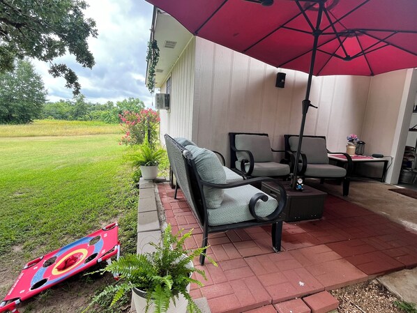 Un espace patio aménagé avec du mobilier d’extérieur, un parasol rouge et une cible.