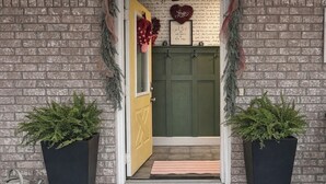 A brick exterior with a green door, two potted plants, a welcome mat, and a sign above the door. - Secluded-Prvt fishing-Close to dwntn-firepit-paddleboat-nature trail-KING bed (Brenham)