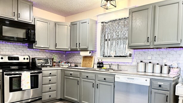 A modern kitchen with grey cabinets, stainless steel appliances, and a purple-lit backsplash. - Secluded-Prvt fishing-Close to dwntn-firepit-paddleboat-nature trail-KING bed (Brenham)
