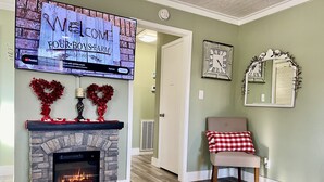 A living room with a stone fireplace, a flat-screen TV mounted above it, a clock, and a decorative mirror on the wall. - Secluded-Prvt fishing-Close to dwntn-firepit-paddleboat-nature trail-KING bed (Brenham)