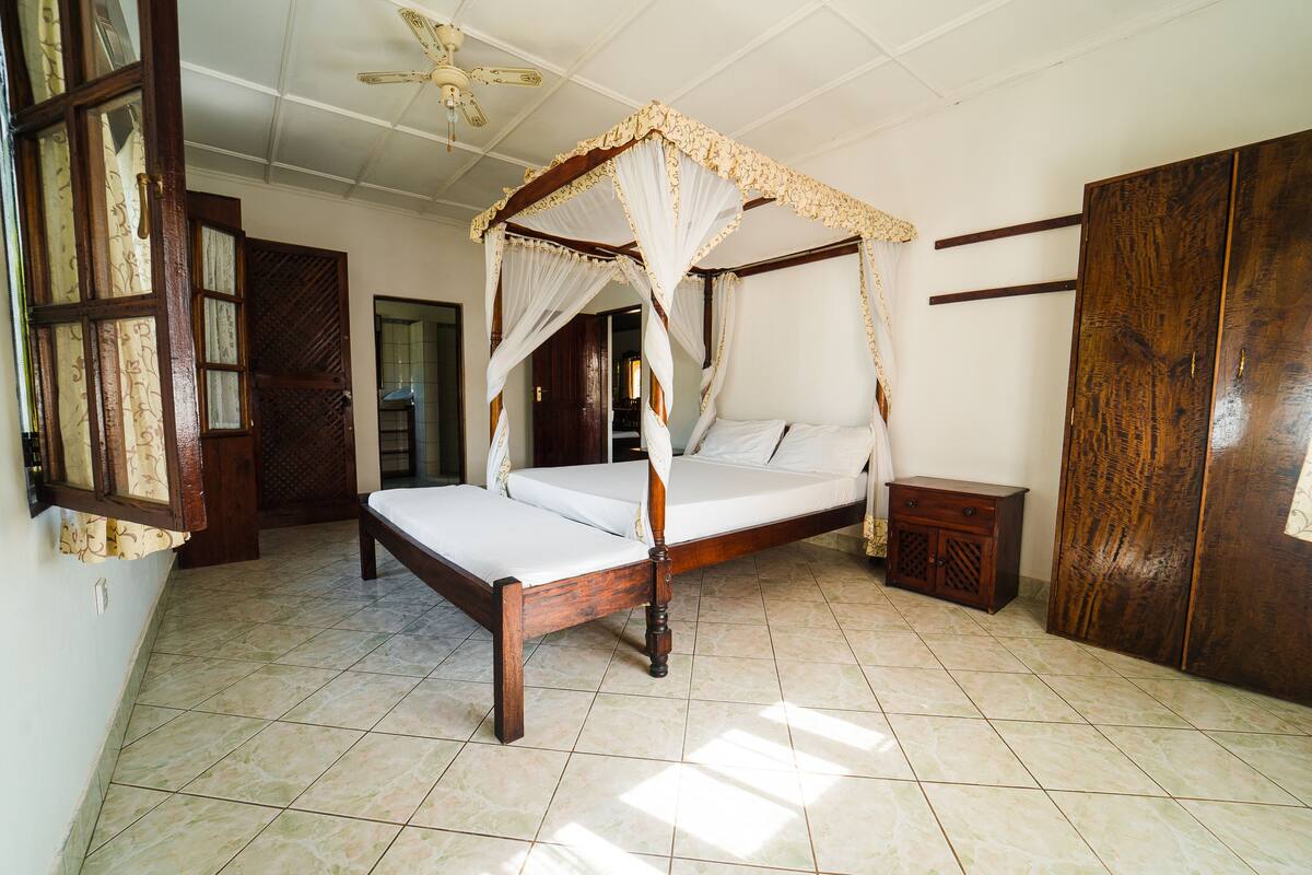 A four-poster bed with a canopy, a wooden wardrobe, and a tiled floor.