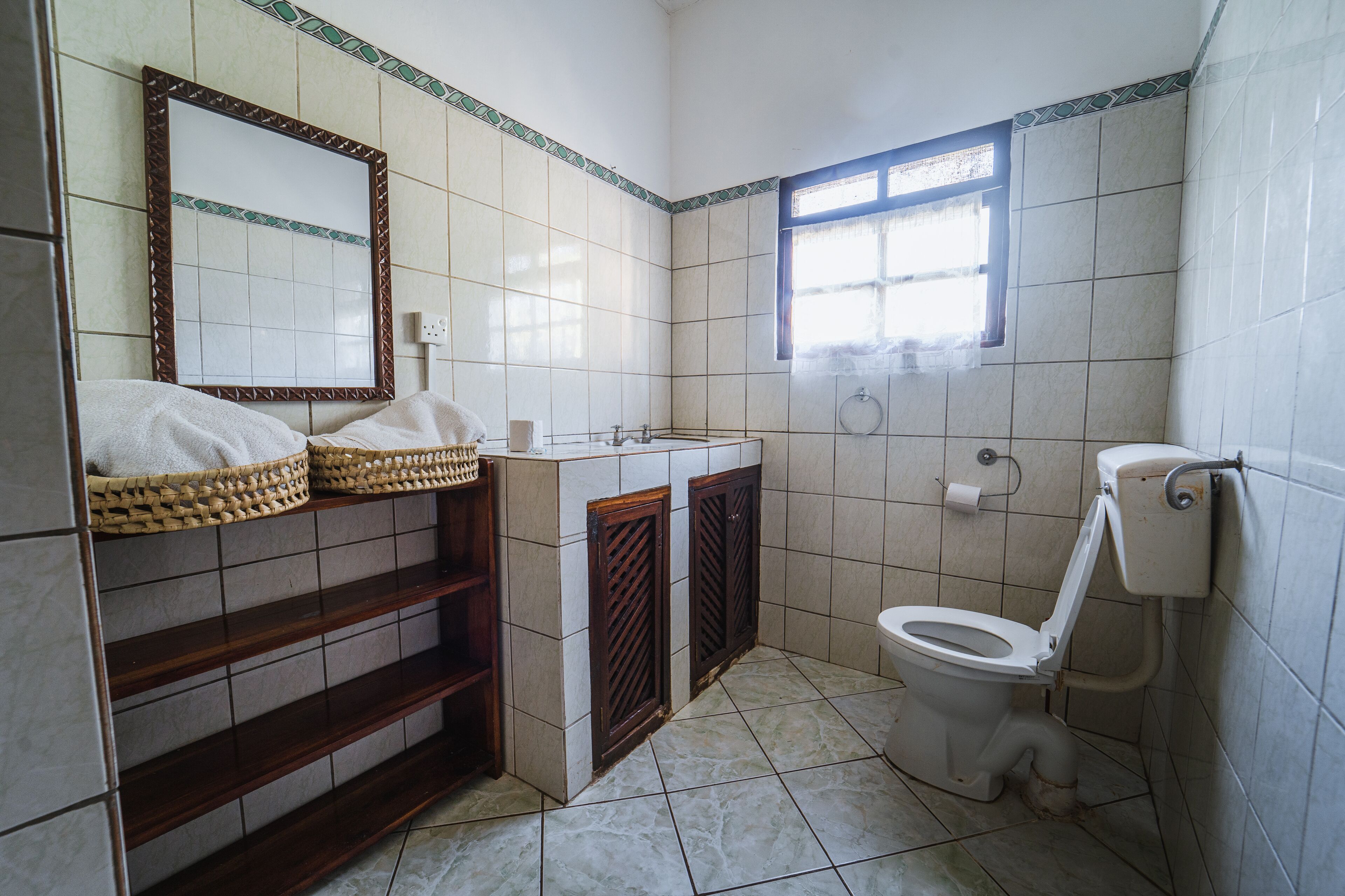 A bathroom with a tiled floor, a sink with a mirror above it, a toilet, and a window.