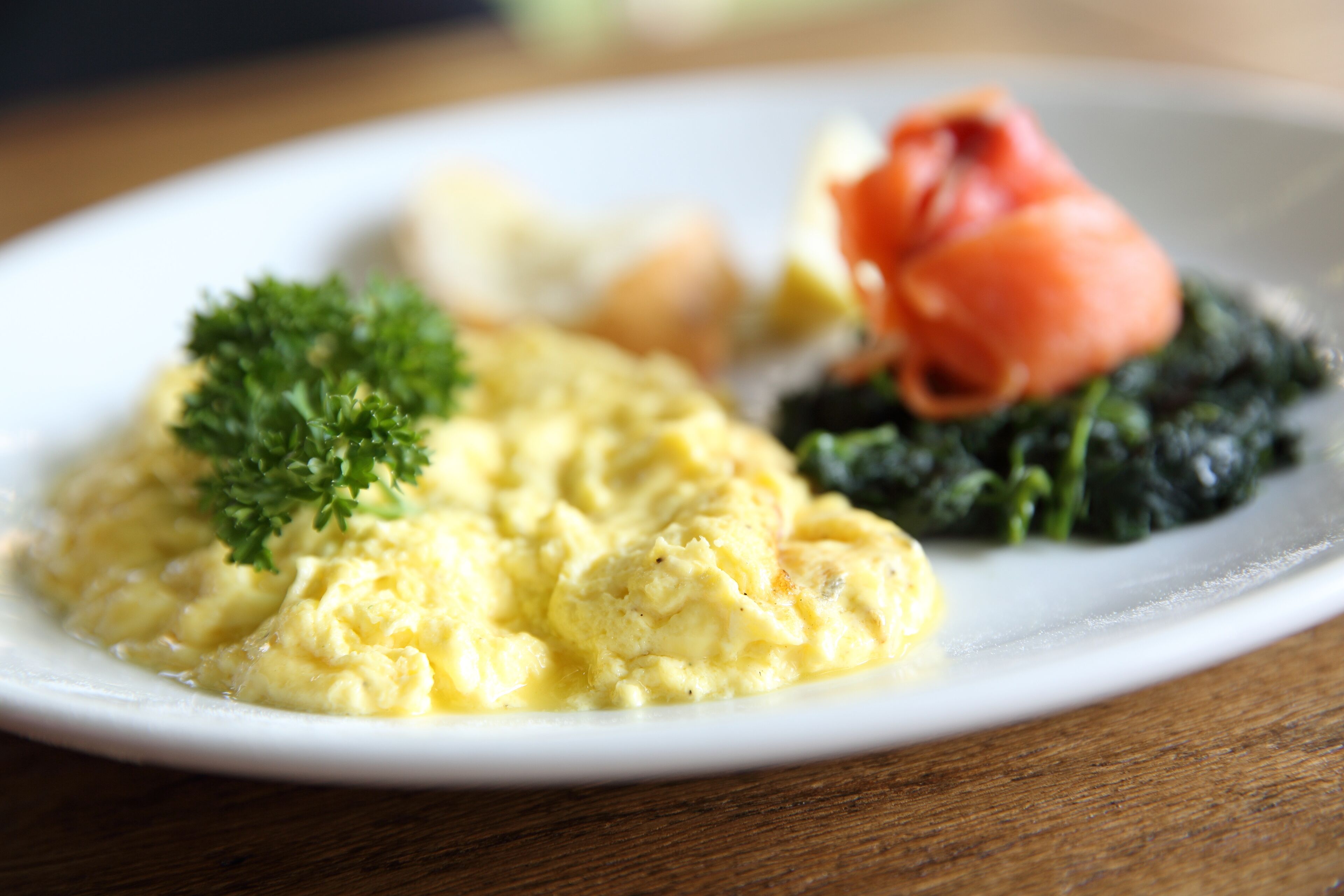 A plate of scrambled eggs garnished with parsley, accompanied by a slice of tomato and a portion of spinach.