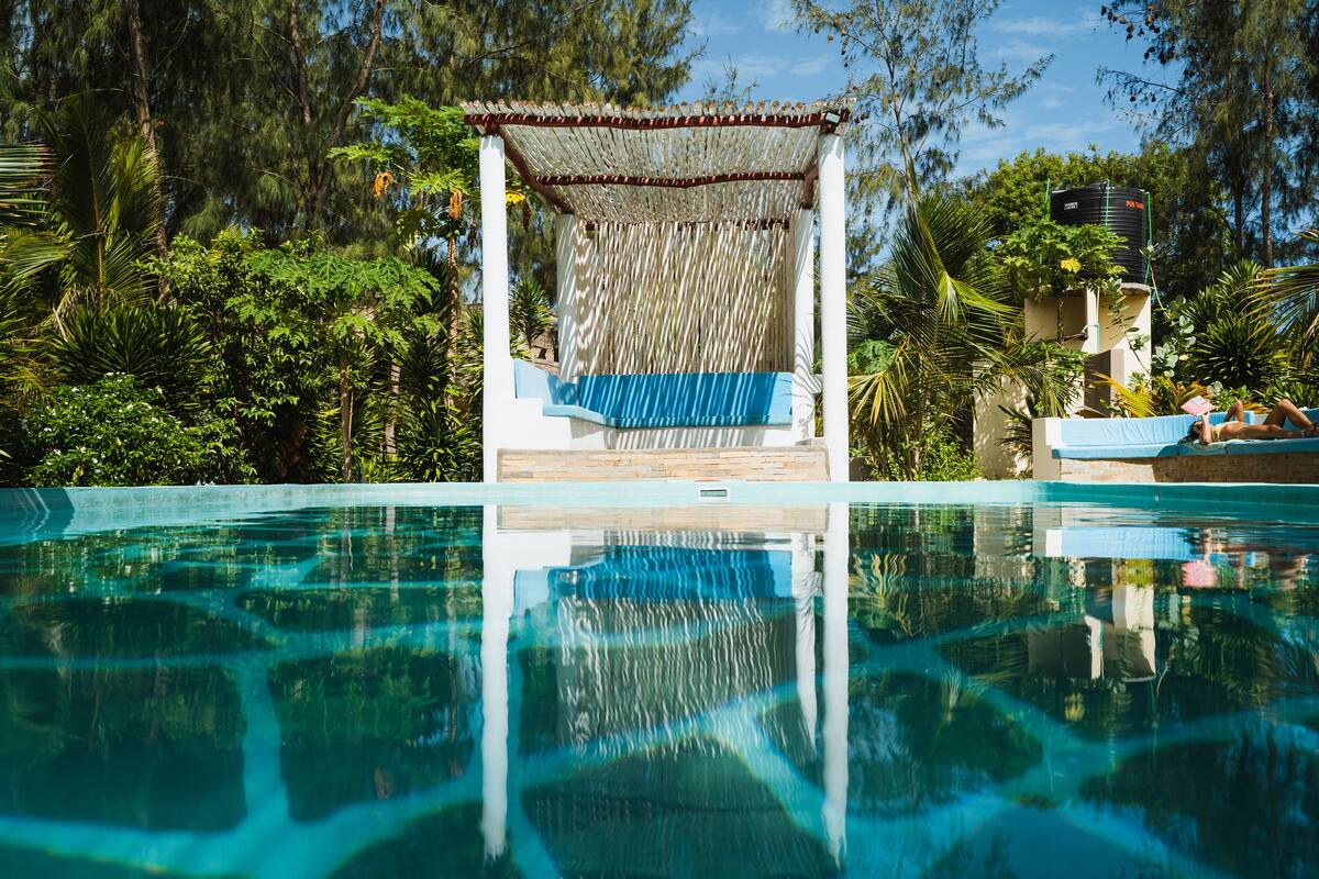 A clear swimming pool with a wooden deck and a covered seating area.