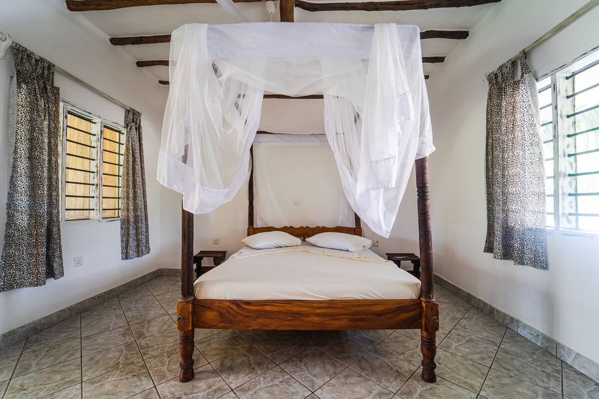 A four-poster bed with a canopy, a wooden headboard, and a tiled floor.