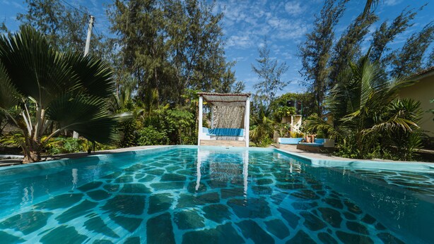 A clear swimming pool surrounded by lush greenery and a gazebo. - GK Palm Resort Watamu (Watamu)
