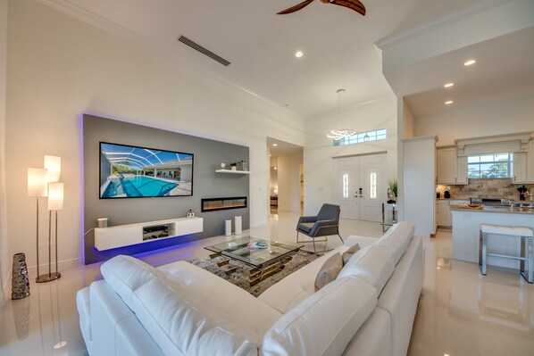 A spacious living room with a white sofa, a glass coffee table, and a flat-screen TV mounted on the wall.