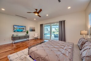 A modern bedroom with a large bed, a ceiling fan, a TV, and a sliding glass door to the outside. - Villa Pure Elegance - new building on water with heated pool/spa, for boaters (Cape Coral)