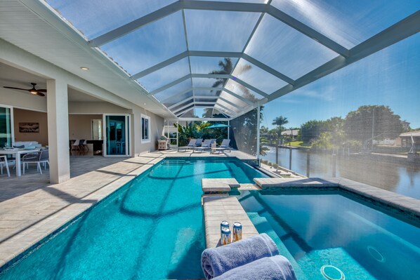 Une piscine à l’eau d’un bleu cristallin, entourée d’un patio abrité agrémenté de chaises longues et de parasols.