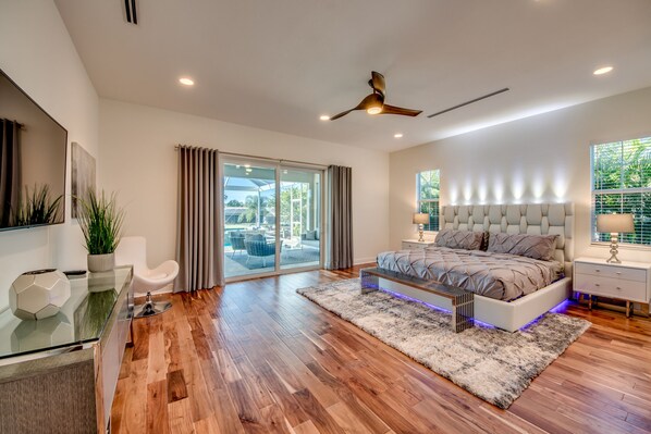 A modern bedroom with a large bed, a ceiling fan, and a view of the outdoors.