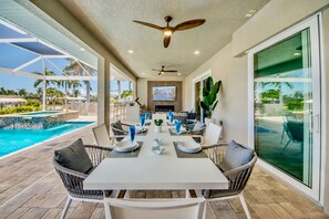 An outdoor dining area with a pool view, ceiling fans, and a large window. - Villa Pure Elegance - new building on water with heated pool/spa, for boaters (Cape Coral)