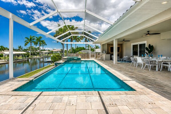 A swimming pool with a covered patio area, outdoor seating, and a view of the surrounding landscape.