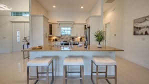 Een moderne keuken met een centraal eiland, barstoelen, roestvrijstalen apparatuur en een groot raam.