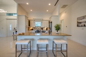 A modern kitchen with a central island, bar stools, stainless steel appliances, and a large window.