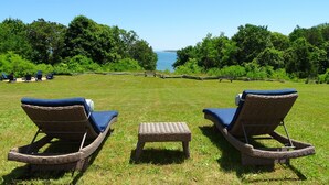 Two wicker lounge chairs with blue cushions facing a grassy area with a view of the sea. - Private Beach - 3 bedroom (Orleans)