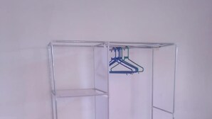 Une armoire en métal transparent, dotée de trois étagères et d’un espace pour suspendre des vêtements.