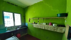 Une cuisine avec des murs verts, une fenêtre, un évier et une étagère remplie d’ustensiles de cuisine.