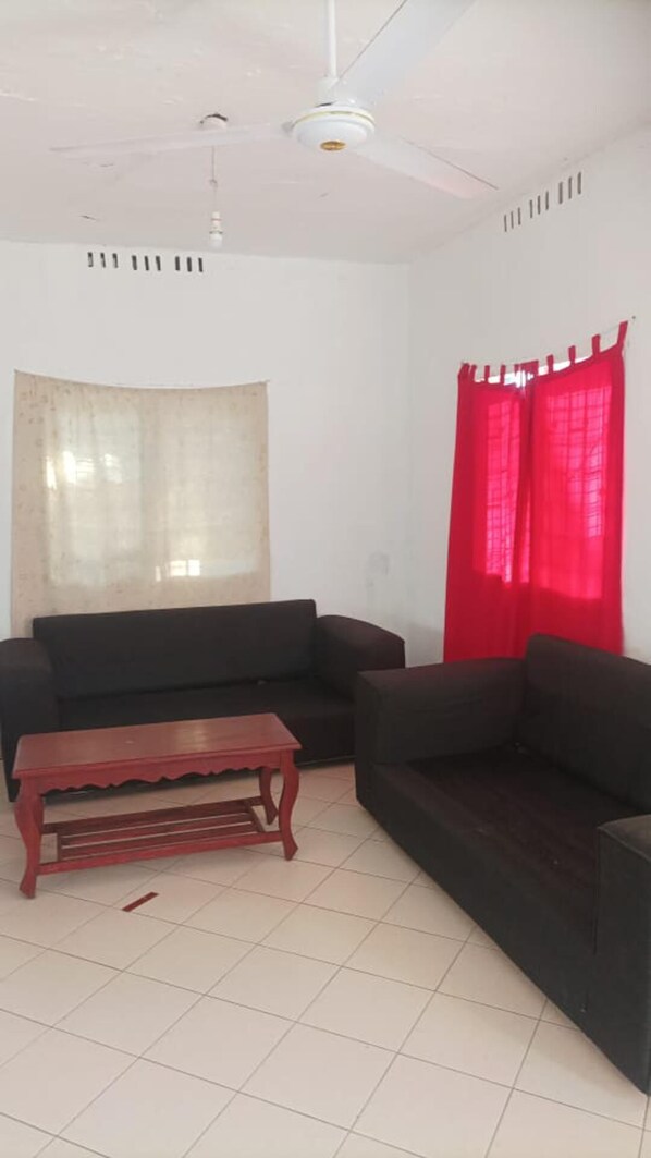 A living room with two dark sofas, a wooden coffee table, a ceiling fan, and a window with red curtains.