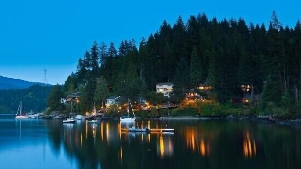 A lakeside property with boats docked, a sailboat, and houses with lights reflecting on the water. - Rustic modern garden level suite (North Vancouver)