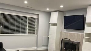 A modern living room with a fireplace, a TV mounted on the wall, and a wooden table. - Rustic modern garden level suite (North Vancouver)