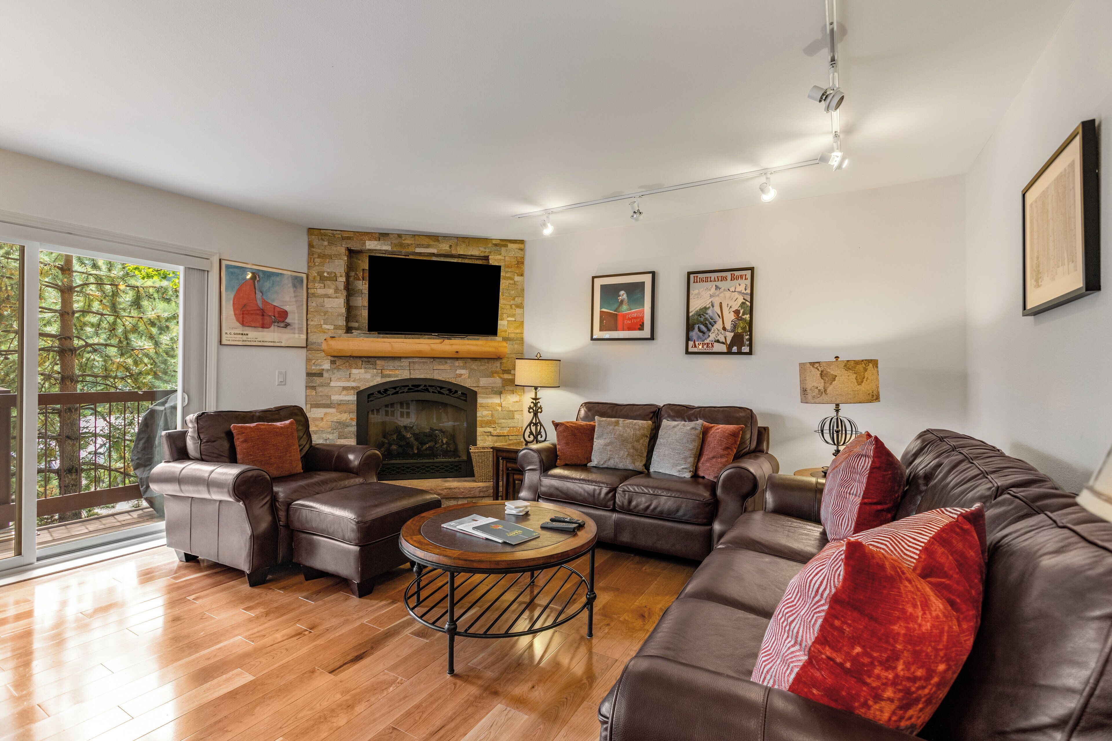 A modern living room with leather sofas, a stone fireplace, and artwork on the walls.
